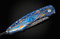 Folding knife with a blue and silver patterned handle on a black background