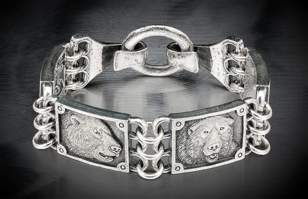 Silver metal bracelet featuring two detailed bear head engravings and an ornate chain link design.