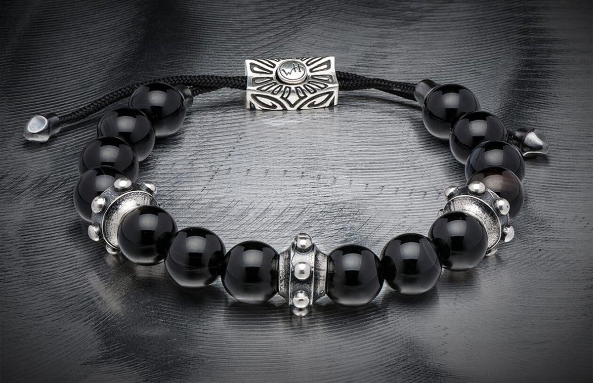 Black sardonyx bead bracelet with silver decorative spacers, a slider charm featuring 'WH' logo, and black braided cord.