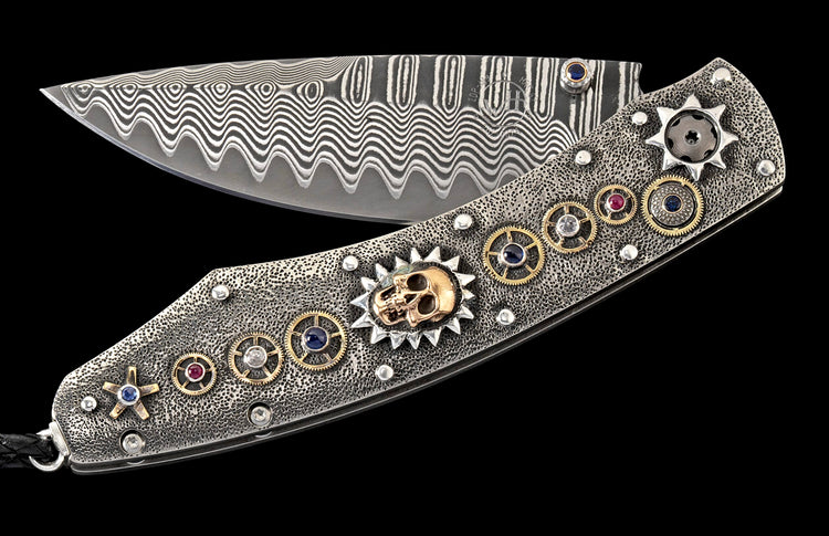 Ornate folding knife with wavy Damascus blade and textured metal handle featuring a gold skull, gears, and multi-colored gems.