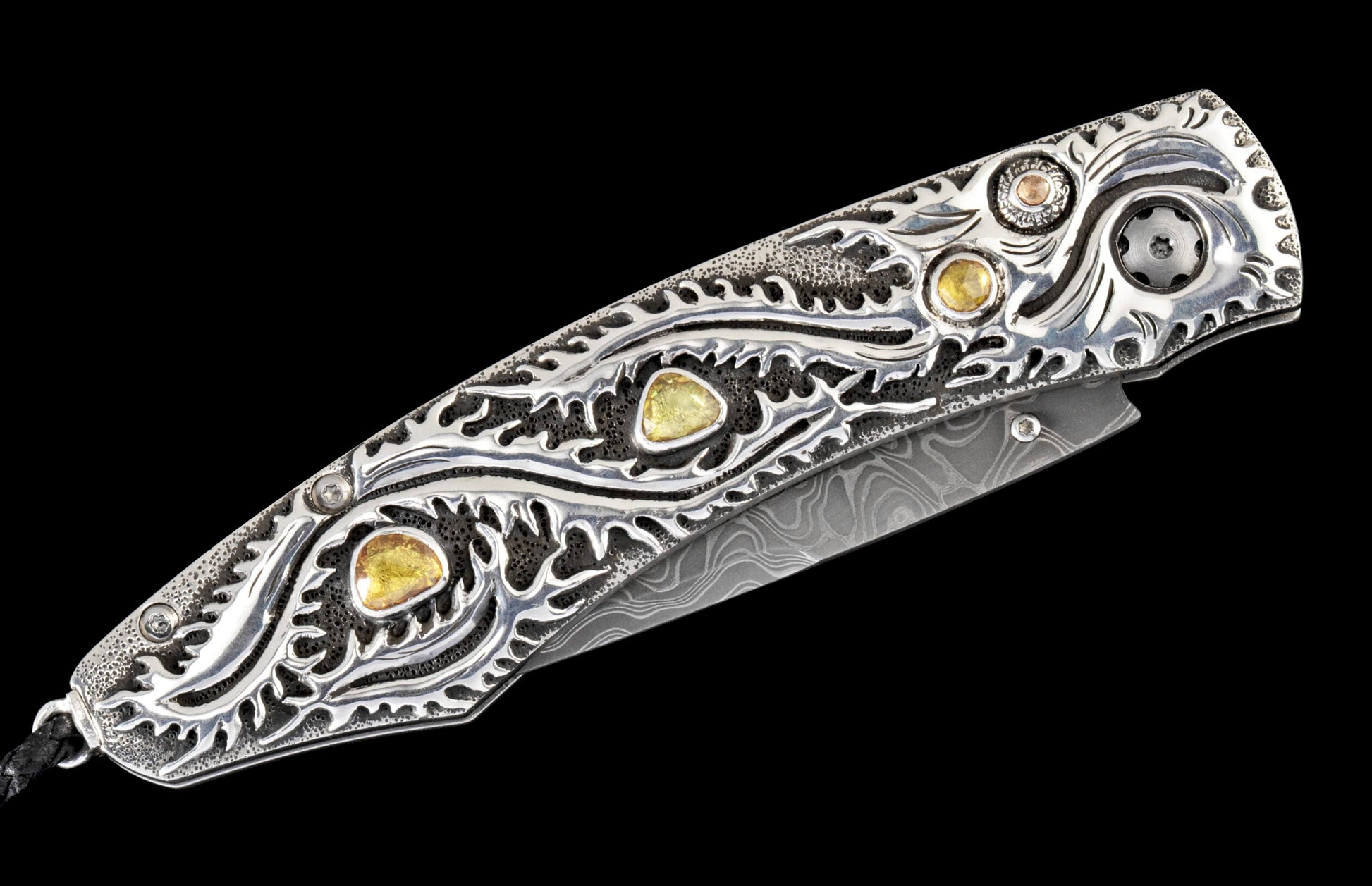Ornate folding knife with silver scrollwork, three yellow gemstones, a black textured handle, and a patterned Damascus steel blade.