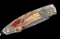 Folding knife with a reddish-beige stone handle, embellished with silver and gold-tone gears, and a visible Damascus steel blade.