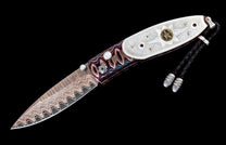 Ornate knife with wavy patterned Damascus blade, iridescent white handle scales featuring a star, and colorful wavy handle sections with a braided lanyard.