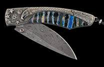 Ornate folding knife with Damascus steel blade and silver handle featuring an eagle head, stars, blue gemstones, and a vibrant striped inlay.