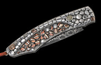 Decorative folding knife handle with polished silver-colored and striped brown-black inlays on a textured background, with a Damascus blade and a leather lanyard.