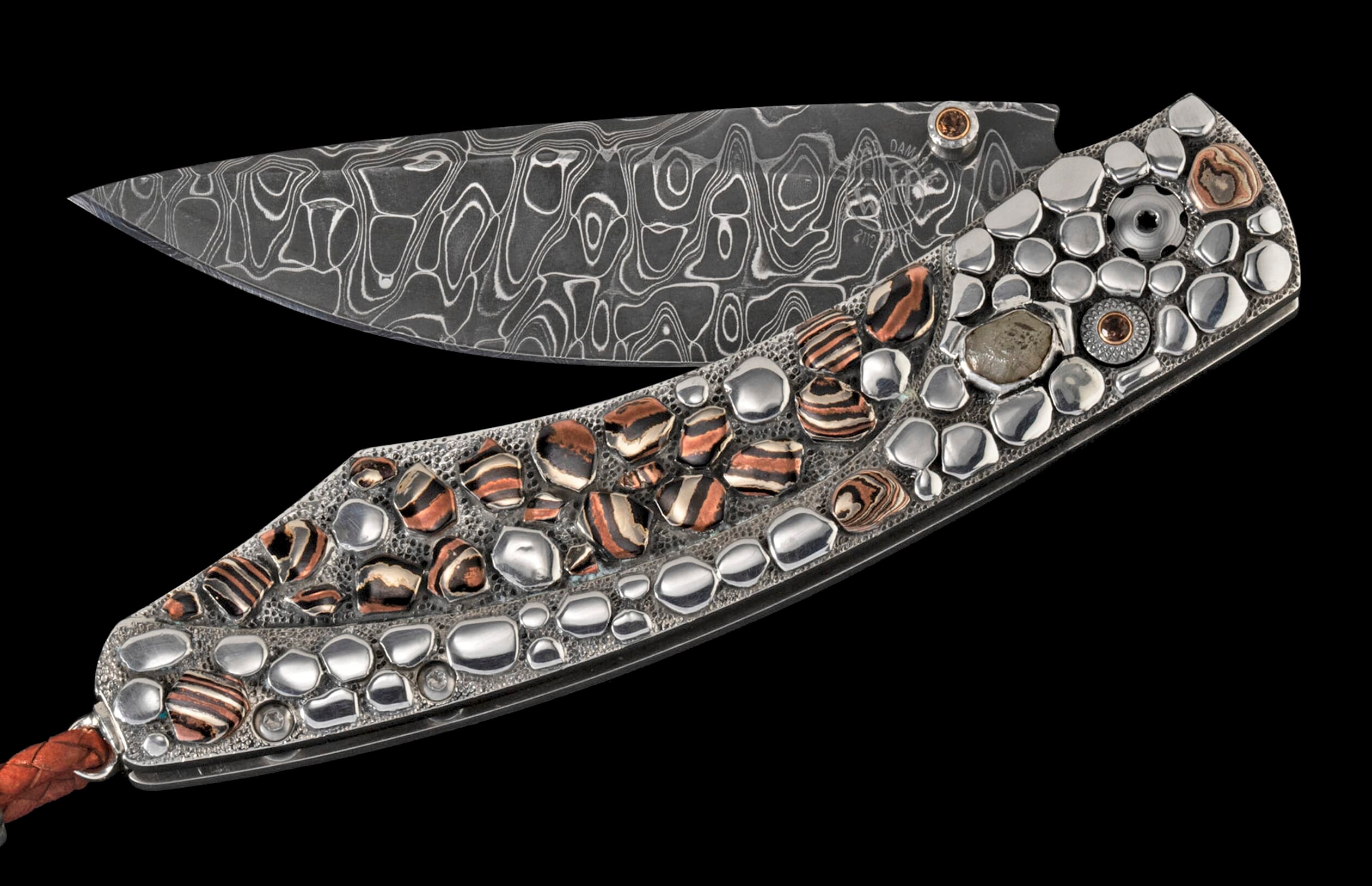 Ornate folding knife with a Damascus steel blade, textured handle inlaid with silver-toned pebbles, striped stones, and a braided lanyard.