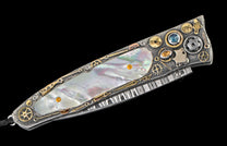 Ornate folding knife with iridescent mother-of-pearl inlay, textured silver metal, gold gears, and colorful gemstones.