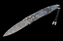 Ornate open knife with wavy Damascus steel blade and silver handle featuring an eagle carving, stars, iridescent abalone inlay, and a braided leather lanyard.