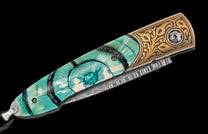 Knife with a teal and white swirling handle, ornate gold engraved bolster, and wavy Damascus patterned steel.
