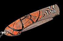 Folding knife with an orange handle featuring a black fractured design and a wavy, multi-toned Damascus blade and bolster.