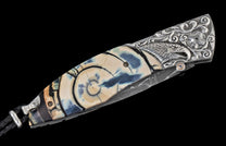 Folding knife with intricately carved silver bolster featuring an eagle head, a patterned ivory handle with blue concentric rings, a Damascus steel blade, and a black leather lanyard.