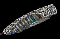 Decorative folding knife featuring an ornate silver-colored handle, vibrant iridescent inlay, and a Damascus blade, accented with red, blue, and clear gemstones.