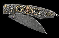 Folding knife with a textured silver-toned handle featuring gold and silver gears, a copper skull, blue and black gems, and a patterned Damascus steel blade.