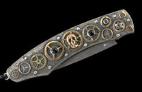 Closed folding knife with textured silver handle, gold gears, a skull, black and blue gemstones, and a Damascus steel blade.