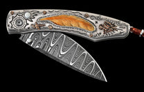 Ornate silver-toned folding knife with a Damascus blade, mother-of-pearl, feather inlay, and engraved motifs.