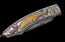 Ornate folding knife with a Damascus blade and silver-toned handle, featuring a carved feather inlay, bird, and cross motifs.