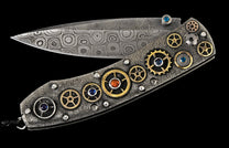 Open folding knife with a patterned Damascus steel blade and a textured handle adorned with golden gears and colorful gemstones.
