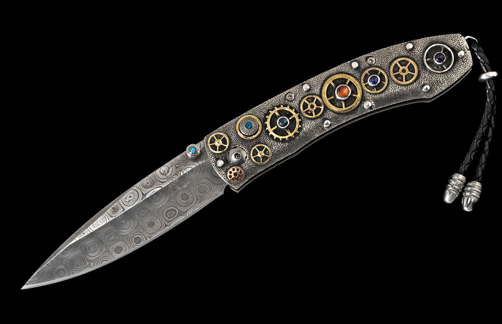 Open folding knife with Damascus patterned blade and a textured handle adorned with gold gears, colorful gemstones, and a braided leather lanyard.