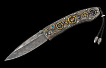 Open folding knife with Damascus patterned blade and a textured handle adorned with gold gears, colorful gemstones, and a braided leather lanyard.