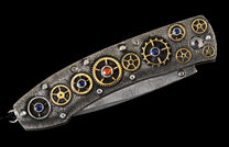 Decorative folding knife with a dark, textured handle featuring gold gears, colorful gemstones, and a patterned Damascus blade.