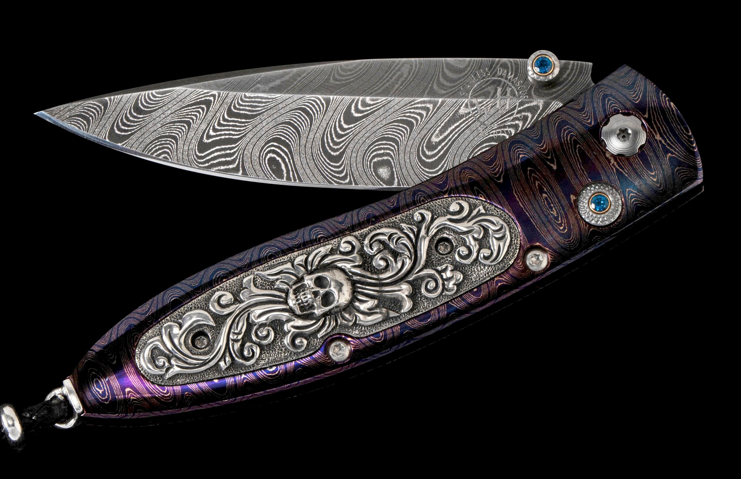 Open Damascus steel knife with purple and blue swirled handle, ornate silver skull design, and blue gemstones.