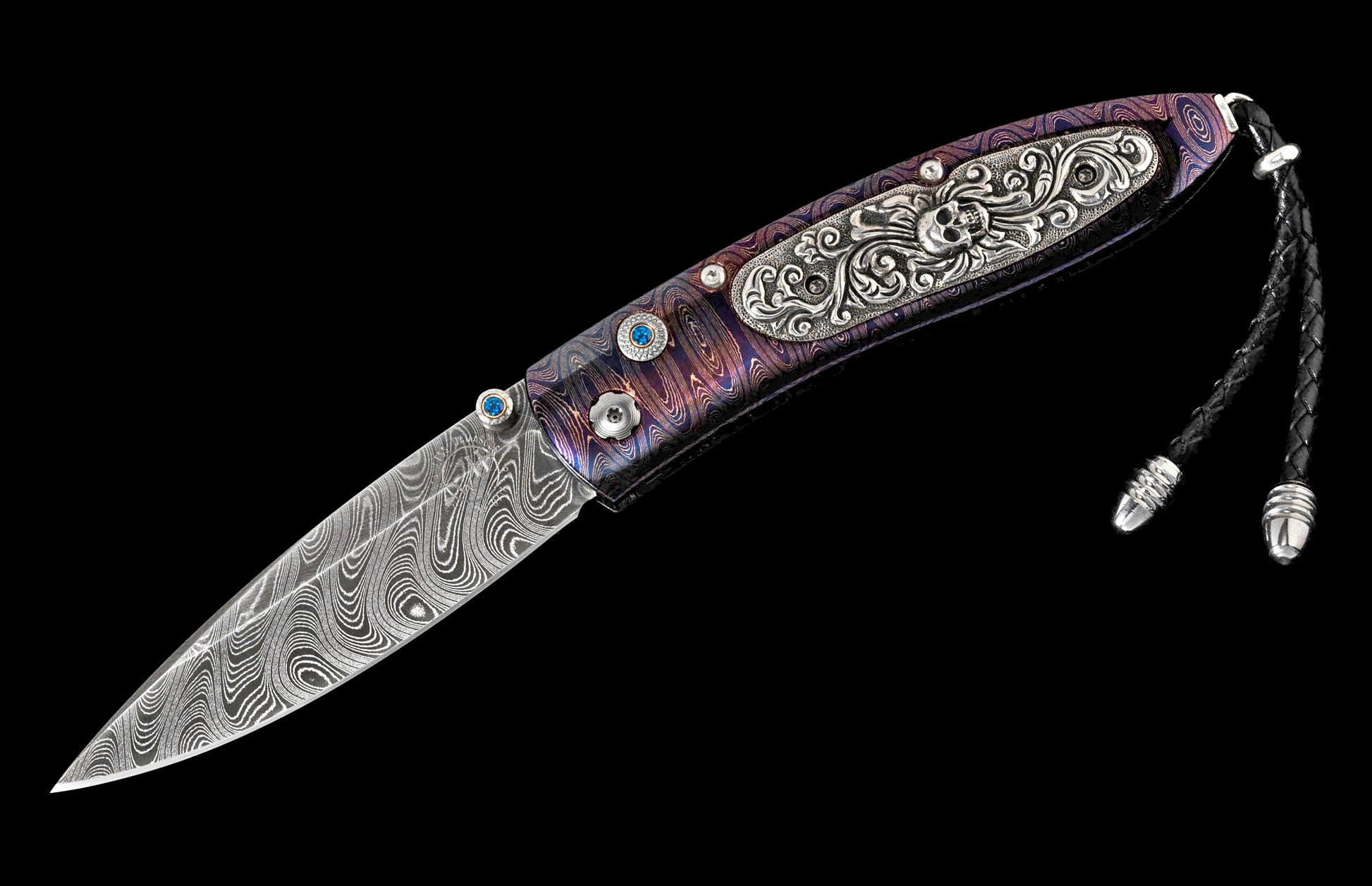 Damascus steel knife with a multi-colored handle featuring blue gems, an ornate skull, and a black leather lanyard.