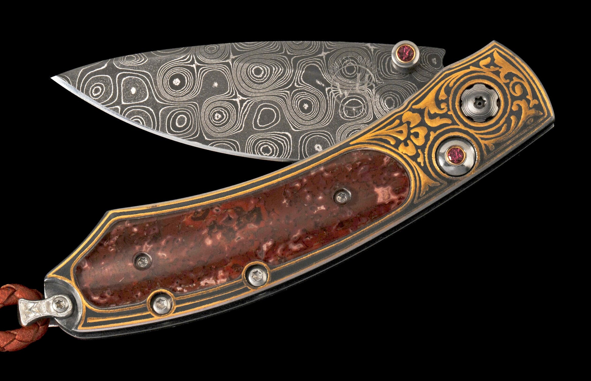 Custom folding knife by WHB, featuring a swirling Damascus blade, reddish-brown stone handle, gold-tone engraving, red gem accents, and a leather lanyard.