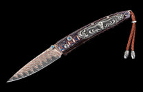 Damascus folding knife with wavy blade, a multi-colored swirling handle, silver steer skull inlay, blue gem accents, and a brown leather lanyard.