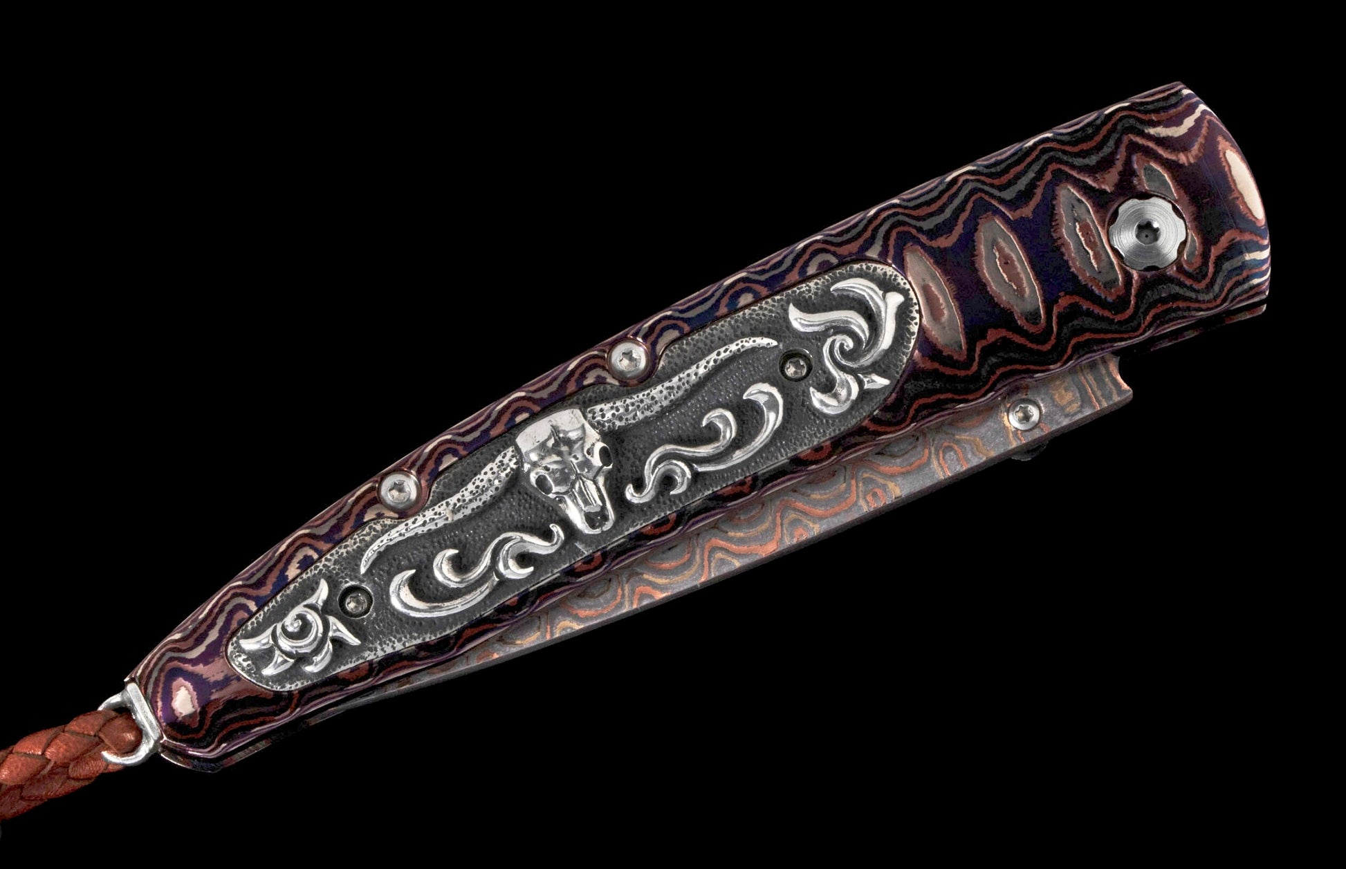 Ornate knife with a purple, brown, and red patterned handle, silver bull skull inlay, and braided leather lanyard.