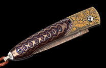 Ornate folding knife with a multi-colored wavy patterned handle, gold floral engraved bolster, and a braided leather lanyard.
