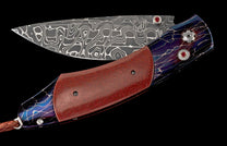 Damascus folding knife with red textured handle, blue-purple lightning pattern, red gem accents, and a braided leather lanyard.