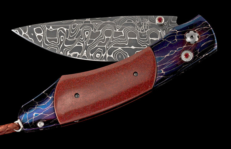 Damascus folding knife with red textured handle, blue-purple lightning pattern, red gem accents, and a braided leather lanyard.