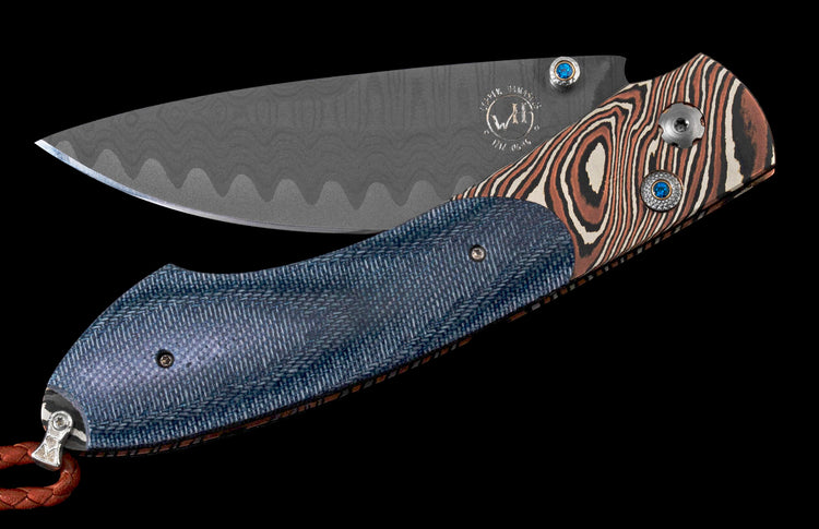 Folding knife with dark gray wavy Damascus blade and blue textured handle with brown swirled accents, "WIENER DAMASCUS" mark, blue gemstones, and leather lanyard.