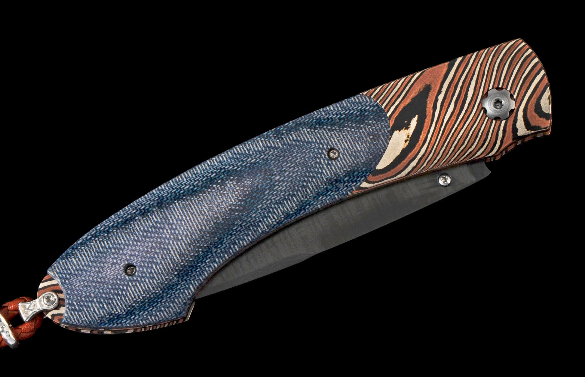 Closed folding knife with a blue denim-textured handle and orange, black, and cream striped pattern, featuring a dark blade and an orange cord lanyard.