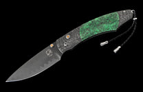 Open folding knife with a wavy Damascus steel blade, textured gray frame, green jade scales, yellow stone accents, and a braided black leather lanyard.