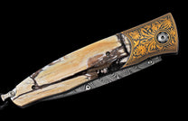 Folding knife with a tan fossilized ivory-like handle, detailed gold floral engraving, and a Damascus steel blade.