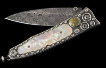 Ornate open folding knife with a swirled Damascus steel blade, iridescent mother-of-pearl handle, sterling silver details, green jasper, and blue sapphires.