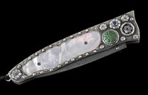 Decorated folding knife with a mother-of-pearl handle inlay, textured silver details, green and blue gemstones, and a Damascus blade.