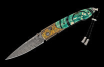 Ornate folding knife featuring a Damascus steel blade and an emerald green and gold engraved handle with a black lanyard.