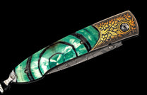 Folding knife with a green and white concentric patterned handle, golden engraved bolster, and a Damascus steel blade.