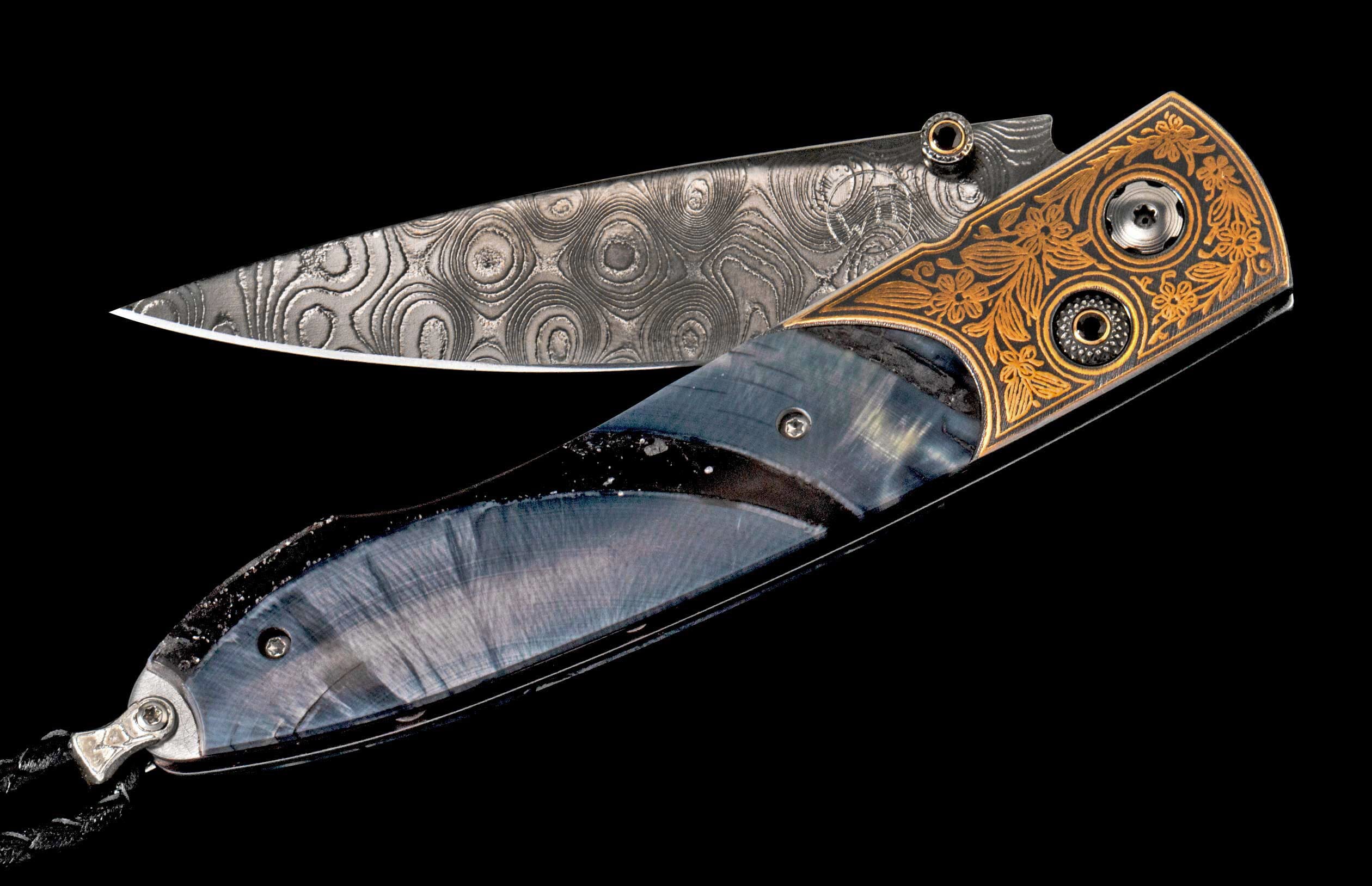 Ornate folding knife with Damascus steel blade, gold floral engraving, and dark blue patterned handle scales.
