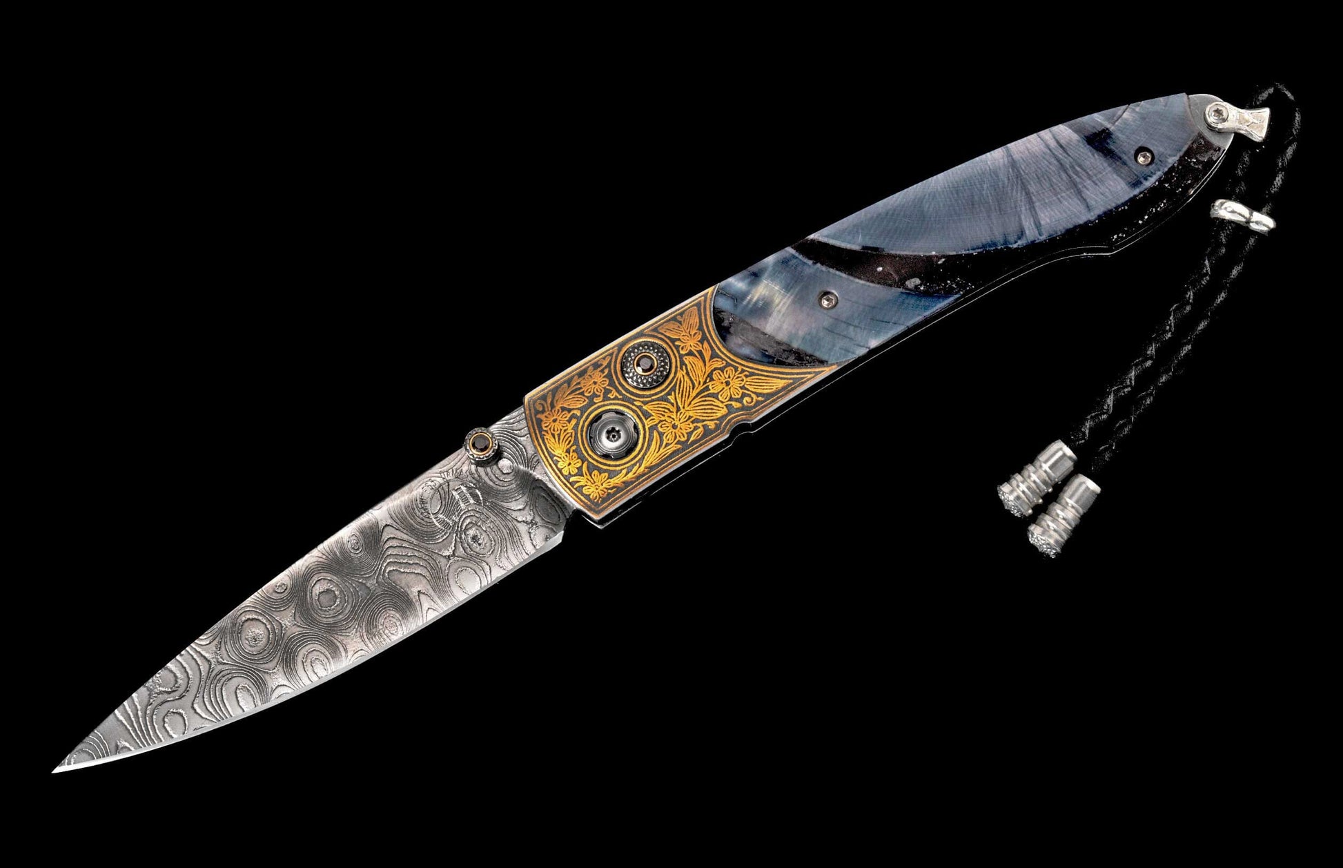 Ornate folding knife featuring a swirling Damascus blade, gold floral engraved handle, dark blue inlay, and black lanyard with silver beads.