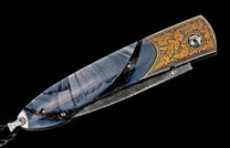 Ornate folding knife with a blue-gray swirling handle, intricate gold floral engravings, and Damascus steel details.
