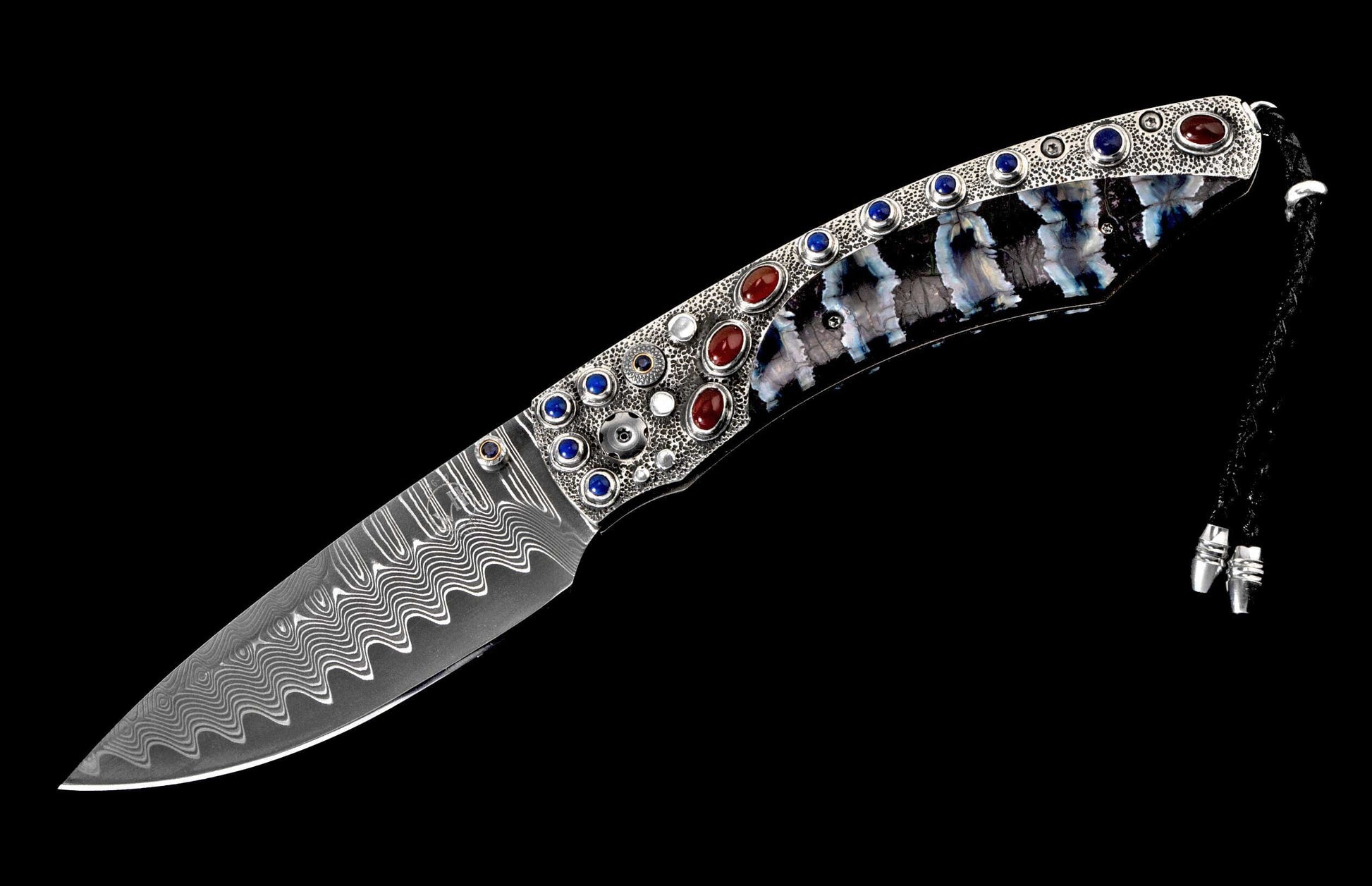Ornate knife with a wavy Damascus blade, textured silver handle featuring red and blue gemstones, marbled shell grip, and braided cord.