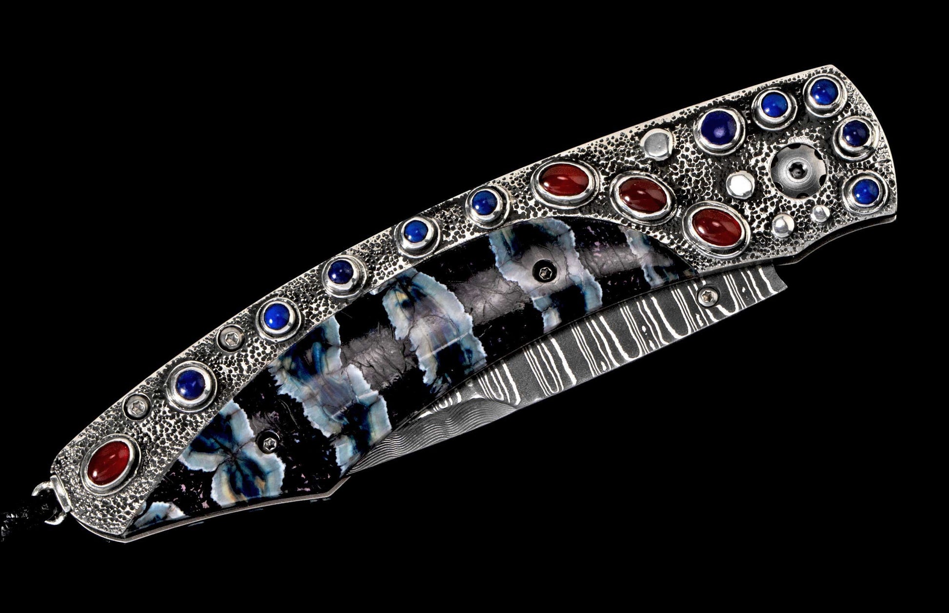 Ornate folding knife with textured silver-toned handle, blue and red gemstones, patterned inlay, and Damascus blade.