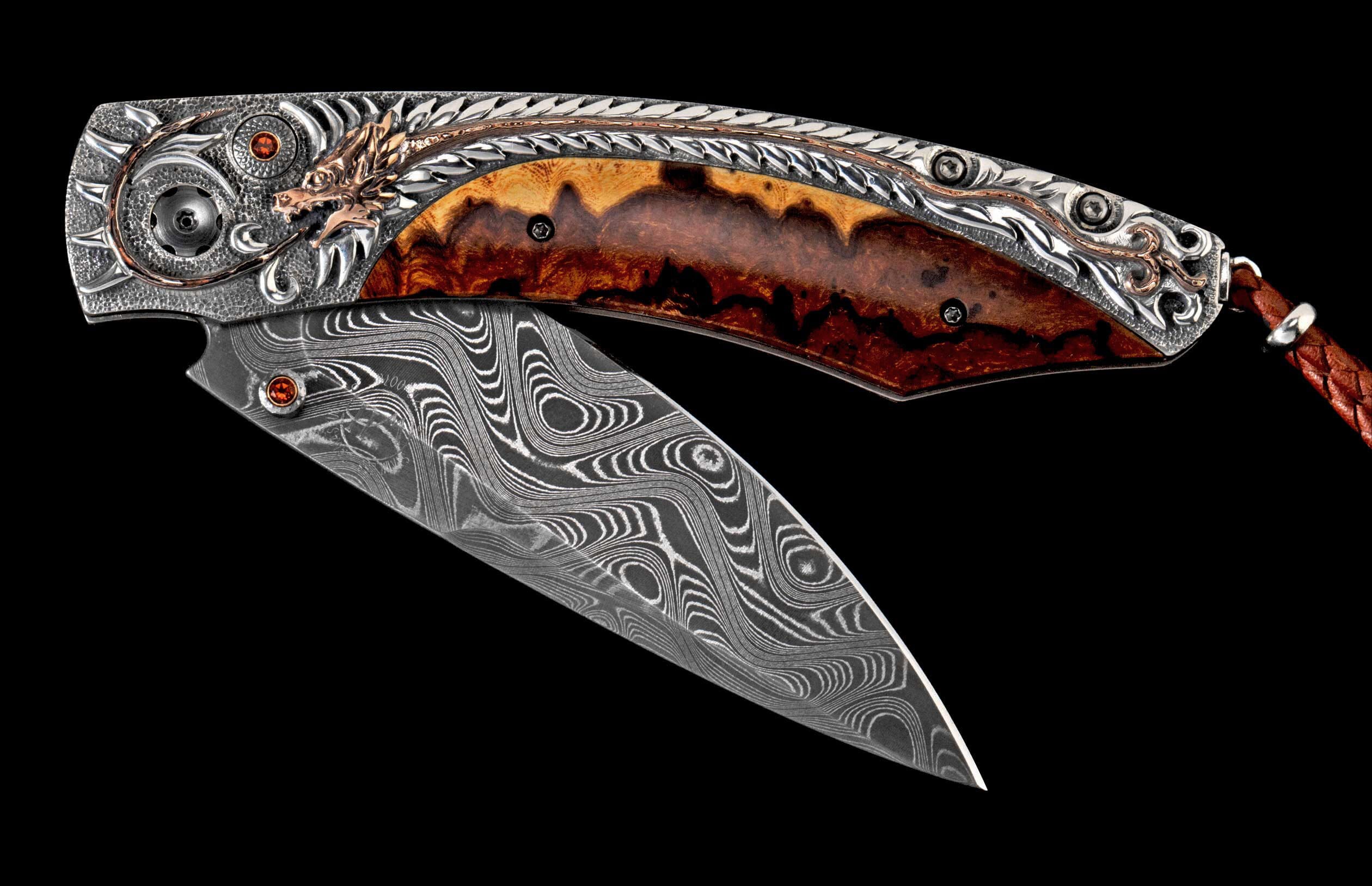 Folding knife, partially open, with a wavy Damascus steel blade and ornate silver handle featuring a bronze dragon, burled wood, red gems, and a leather lanyard.