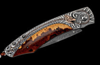Ornate folding knife with a silver-toned handle featuring a copper dragon and sun motif, two-toned wood scales, and a Damascus steel blade.
