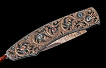Ornate folding knife with rose gold filigree, colorful gemstones, and a patterned Damascus steel blade.