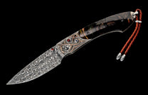 Ornate folding knife featuring a swirling Damascus blade, textured bolster with red and blue gemstones, and a dark striped handle with a brown leather lanyard.