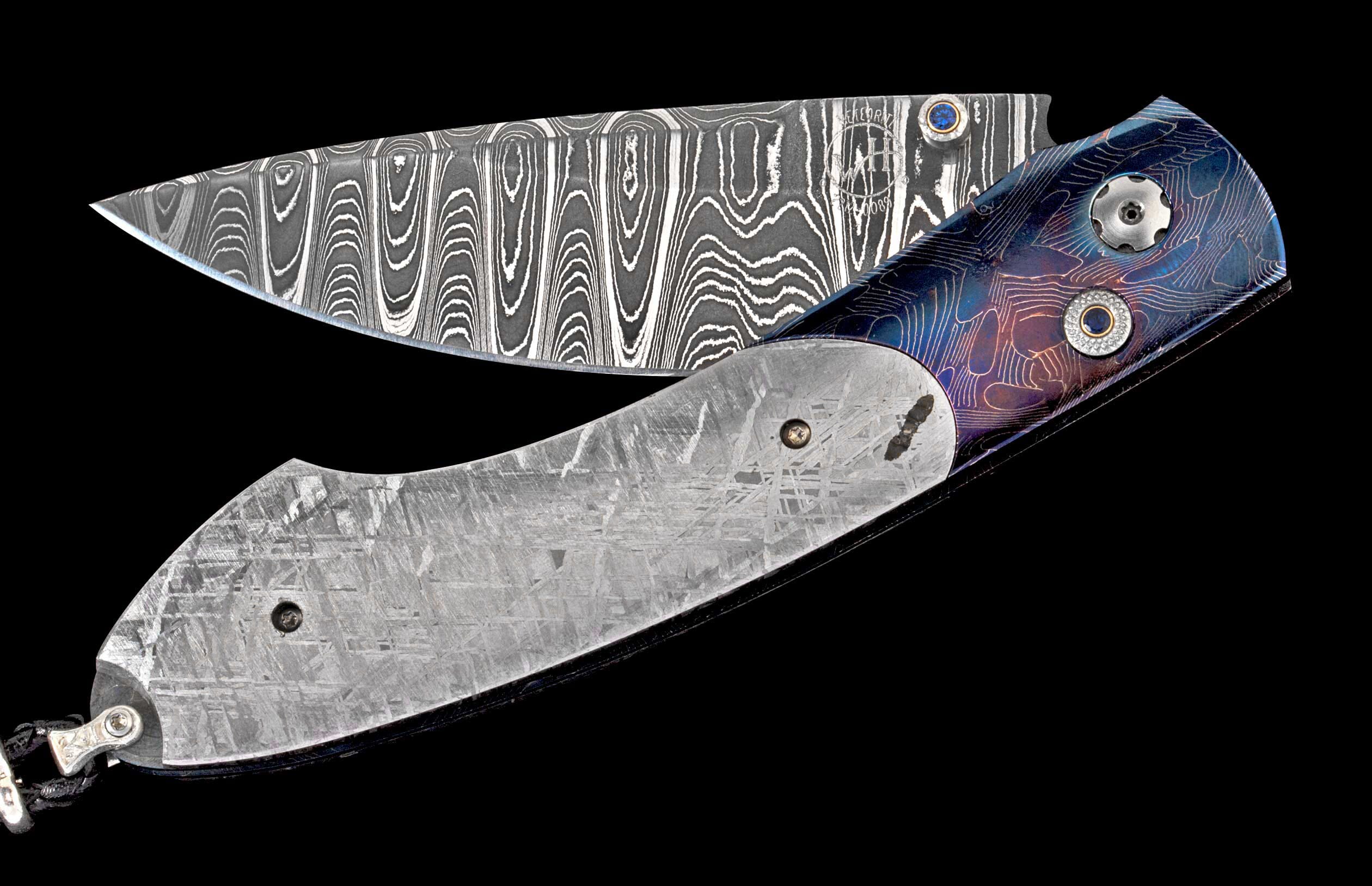 Partially open folding knife with Damascus blade and blue-purple titanium handle featuring meteorite inlay and a sapphire pivot.